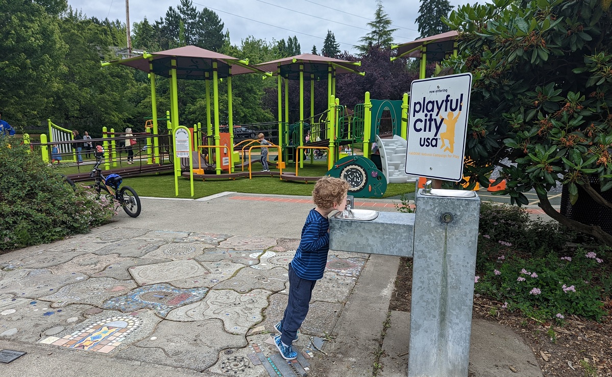 A boy drinking from the drinking fountain at the new Train Park playground at Mercer Island’s Mercerdale Park